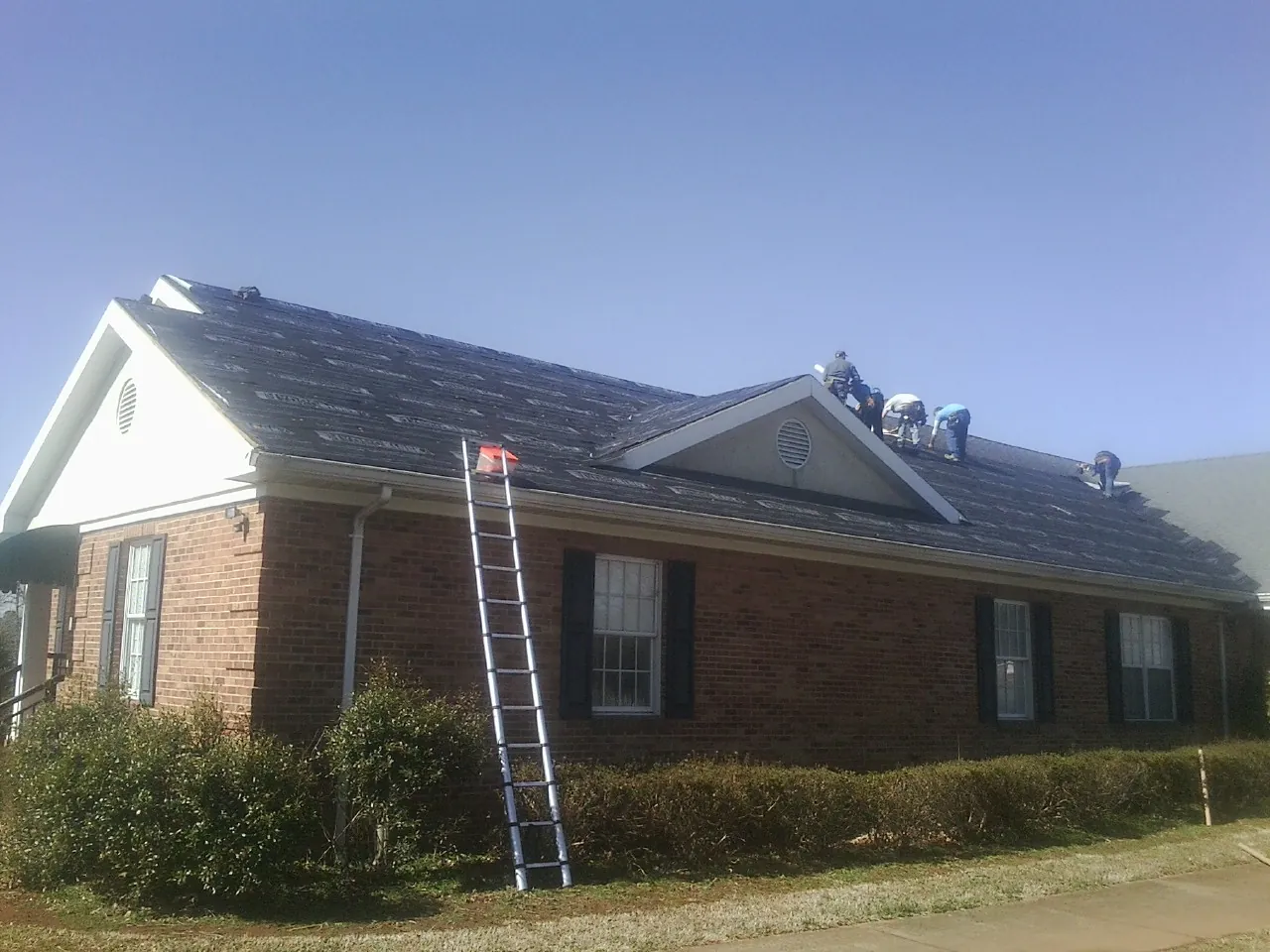 Crew tearing shingles off a brick ranch roof with a ladder set — Metal Roof Repair work by our crew in Martin